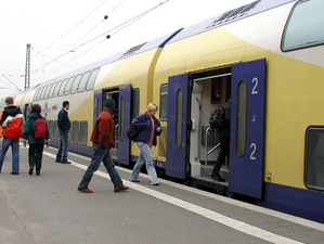 Fahrgäste steigen in gelb-blau-weißen Zug ein