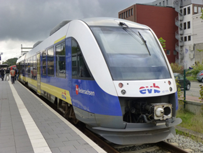 Moderner weiß-blauer Zug der EVB schräg von vorne nach rechts fahrend