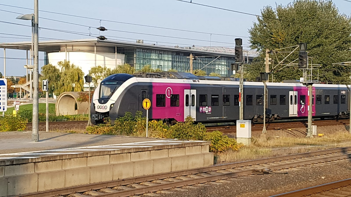 Rosa-grau weisser enno Zug bei der Einfahrt an einen Bahnsteig