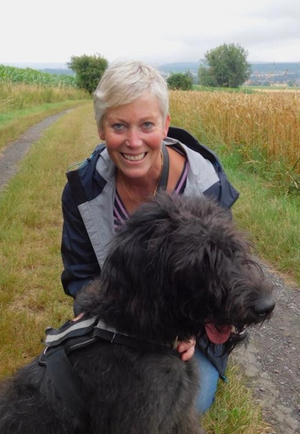 Frau Haack knieend hinter Ihrem mittelgroßen Hund Monty bei einem Spaziergang auf einem Feldweg 