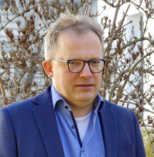 Porträt Ralf Hoopmann im Freien mit Zweigen im Hintergrund