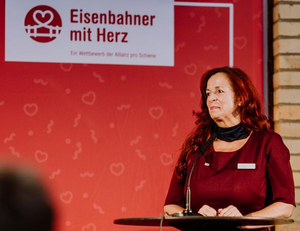 Manuela Burkhardt von DB Regio auf dem Podium an einem Stehtisch bei der Verleihung der Auszeichnung "Eisenbahner mit Herz 2021" durch den Verein" Allianz pro Schiene" an sie.