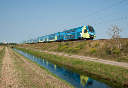 Moderner gelb-türkis-blauer Zug der Westfalenbahn von links nach rechts fahrend