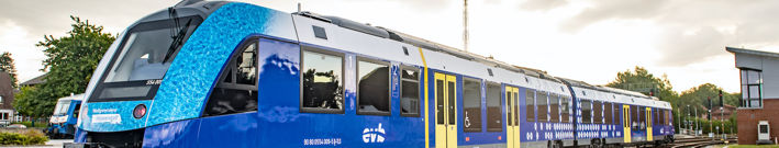 Türkis-blau-gelb-weiser Wasserstoffzug mit Logo der evb (Eisenbahnen und Verkehrsbetriebe Elbe Weser) von rechts nach links fahrendWasserstoffzug mit Logo der evb (Eisenbahnen und Verkehrsbetriebe Elbe Weser) von rechts nach links fahrend