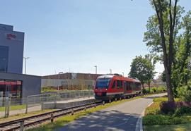 Foto der Ilmebahn vom neuen Haltepunkt BBS/PS-Speicher mit einem roten einteiligen Fahrzeug, das die Ilmebahn betreibt.