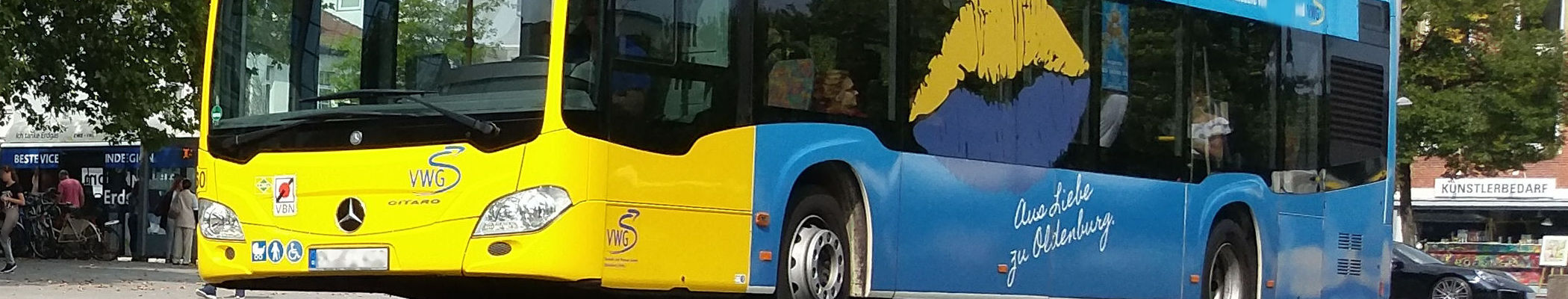 Unterer Ausschnitt eines gelb-blauen umweltfreundlichen Oldenburger Busses in Front- und Seitenansicht im Stadtverkehr