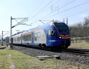 Der Zug von cantus - in blau, grau und orange - einem SPNV-Betreiber im Nordhessischen Verkehrsverbund (NVV) von links nach rechts fahrend in grüner Umgebung