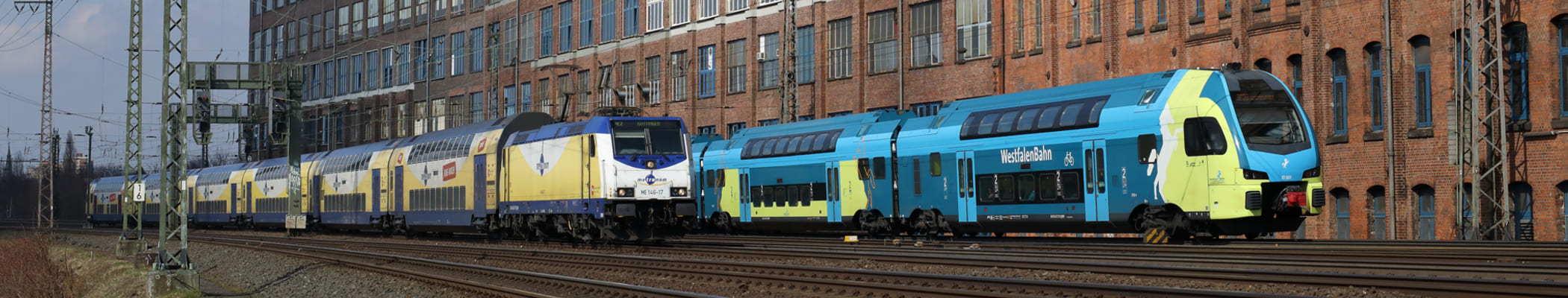 blau gelbe Westfalenbahn und gelb blauer metronom fahren parallel aneinander vorbei